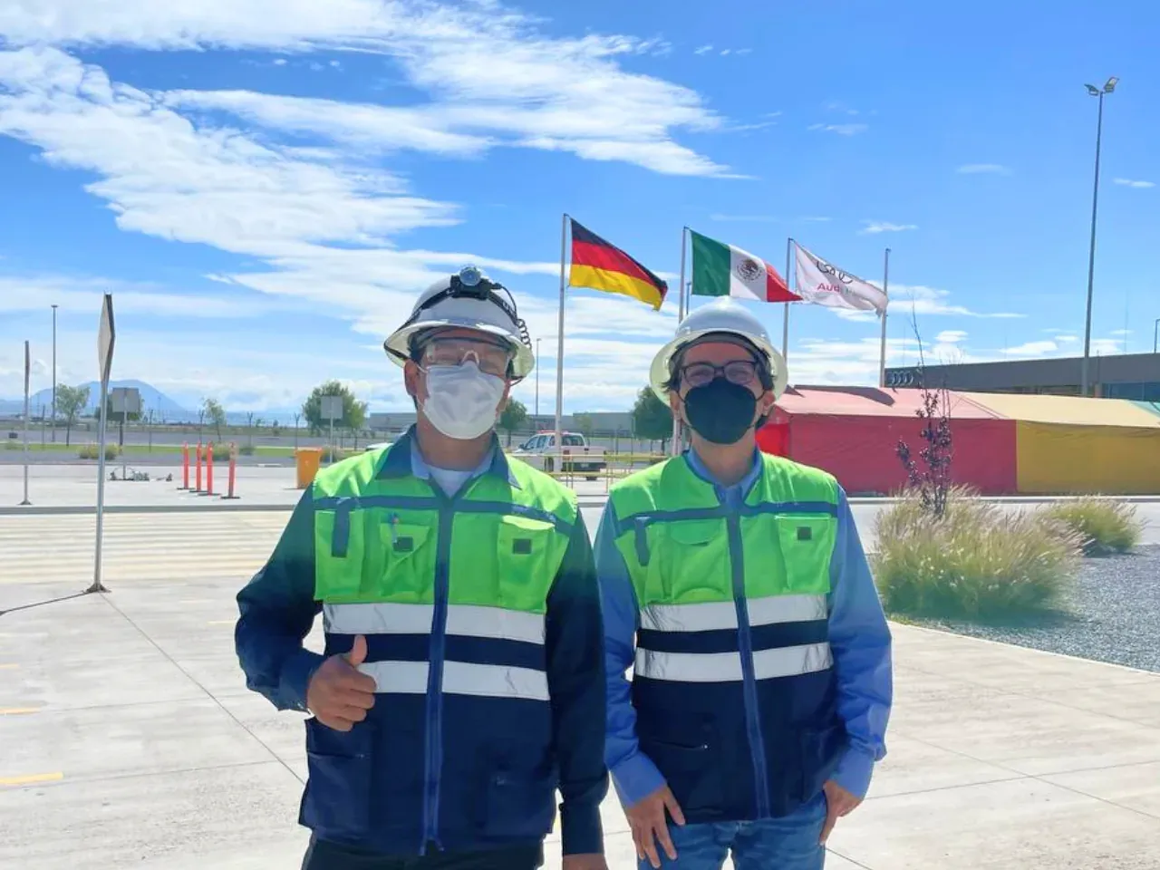 Dos ingenieros de iT Power Systems con casco, careta y chaleco reflejante en el acceso a una planta automotriz donde ejecutan trabajos eléctricos