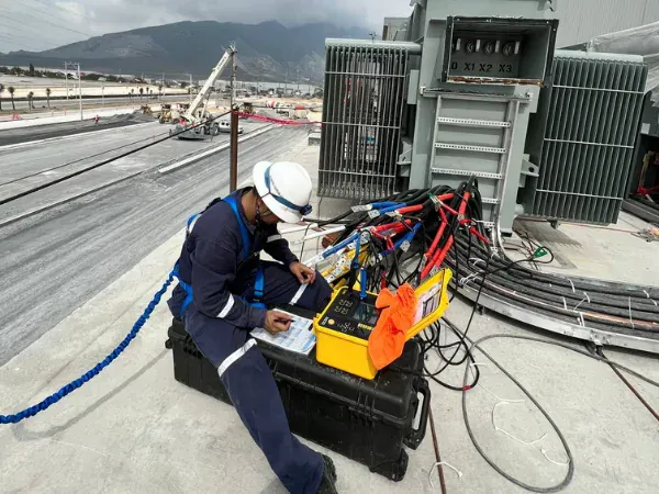 Técnico de iT Power Systems registrando lecturas junto a un equipo de prueba conectado a las boquillas de baja tensión X1, X2 y X3 de un transformador en sitio