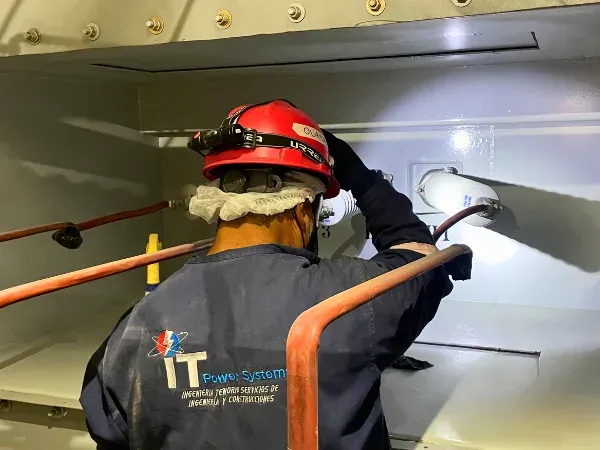 Técnico de iT Power Systems inspeccionando y limpiando barras de cobre con lámpara dentro del compartimento de un tablero eléctrico